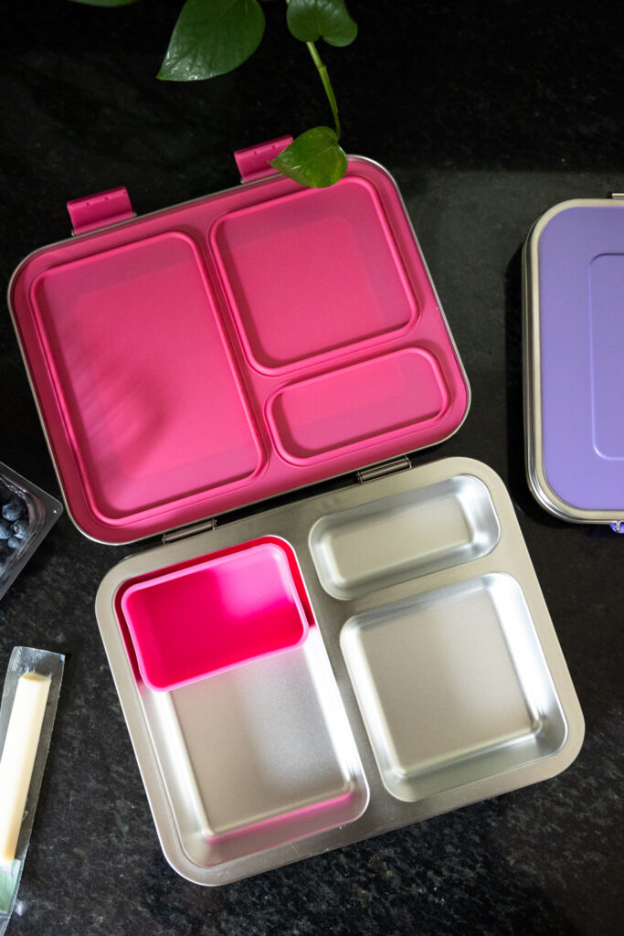 A pink-lidded stainless steel Bentgo kids lunch box sits open on a granite countertop, showing the removeable silicone container and each section, photographed by Raleigh NC candid family photographer