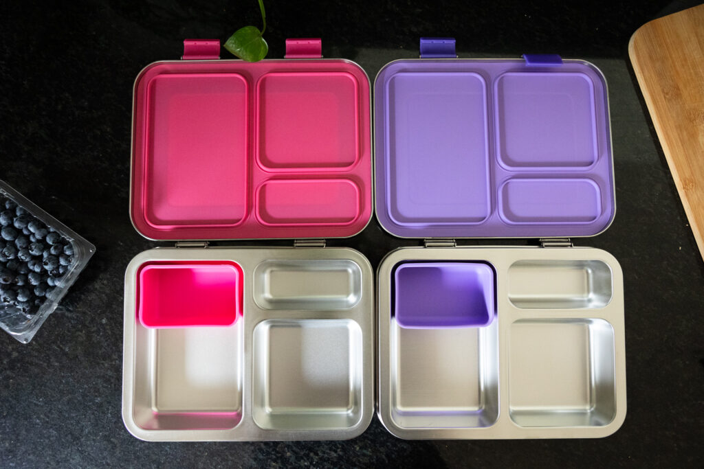 Side-by-side view of open Bentgo Kids stainless steel leak-resistant lunch boxes in pink and purple, each with removable silicone compartments for fresh snacks and meals, Raleigh NC family product photography