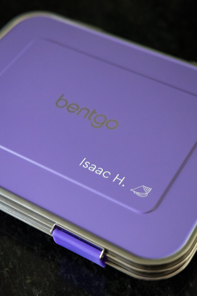 Customized stainless steel lunch box in purple with name personalization including Isaac H. and a seashell design, photographed by Raleigh candid family photographer