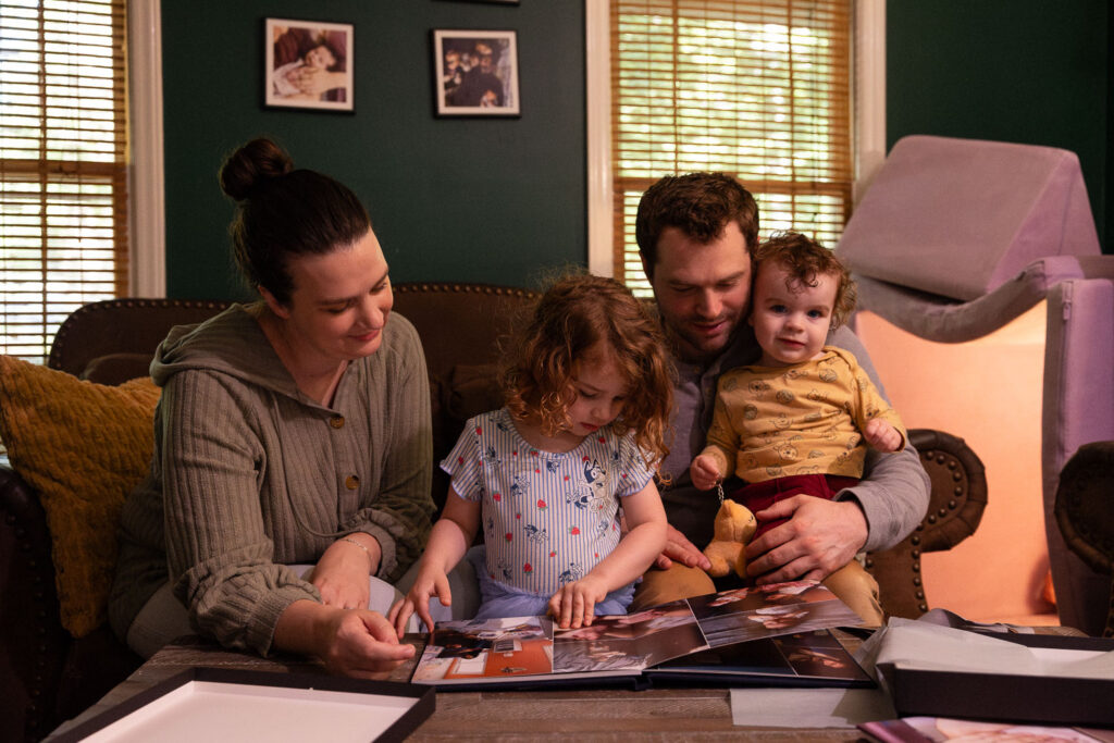 Family of four looks at baby boy's photo album from his first year photo sessions in Raleigh