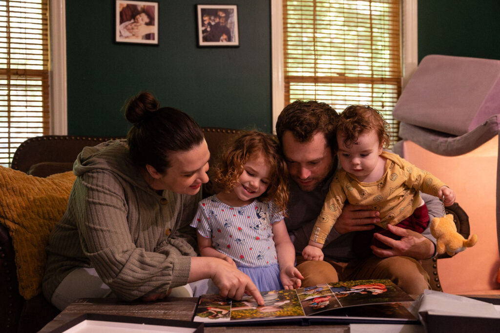 Family of four looks at baby boy's photo album from his baby's first year photography experience in Raleigh