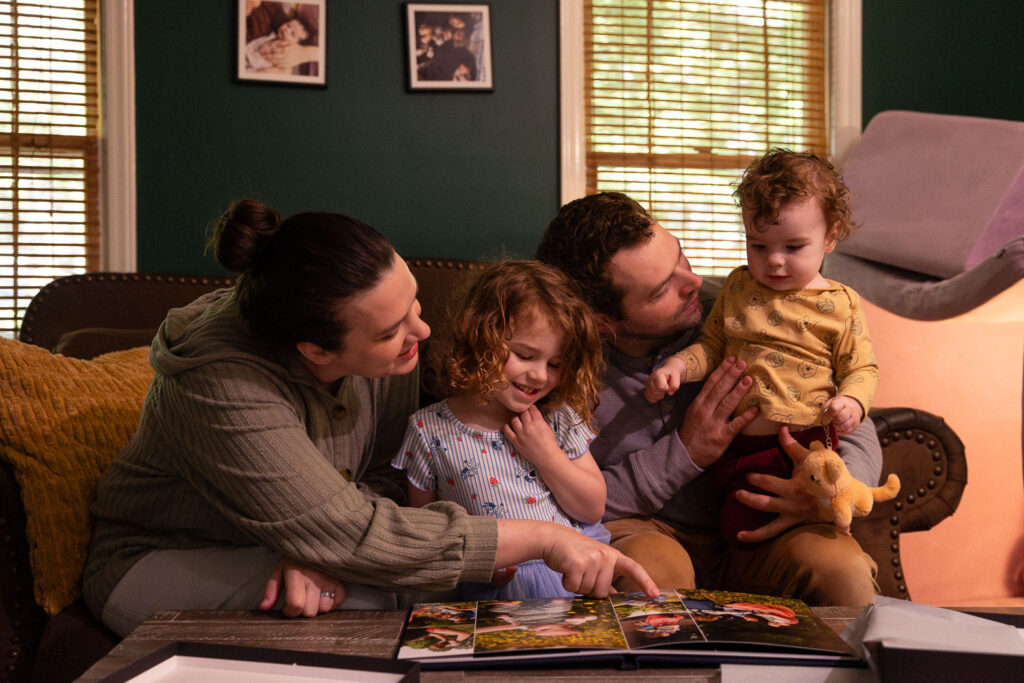 Family of four looks at baby boy's New Life Collection photo album from his baby's first year photo sessions in Raleigh