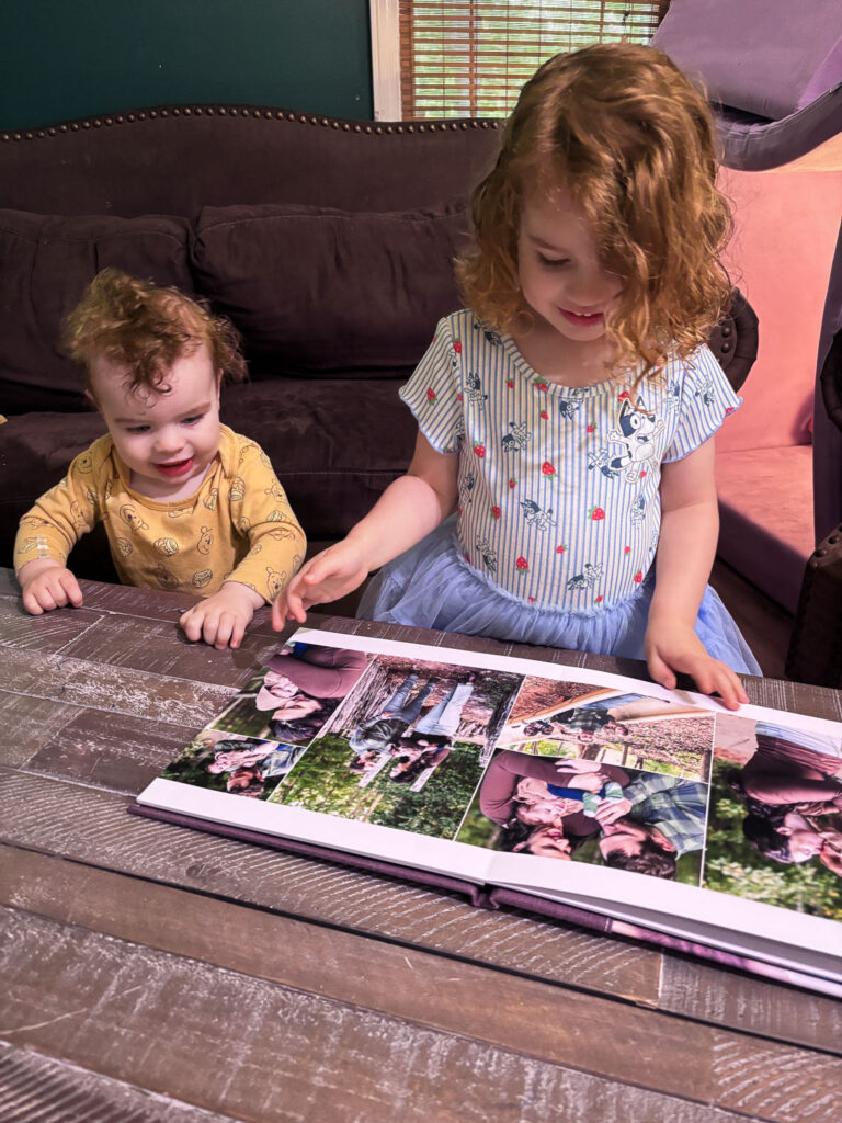 Keepsake photo album for baby's first year photo collection in Raleigh, toddler girl shows her baby brother her photo album