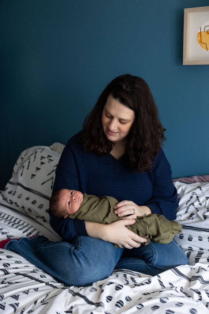 Natural newborn photos in Raleigh, NC, mom smiles at newborn son while holding him in green swaddle blanket