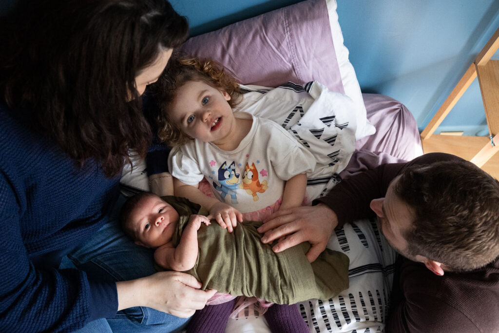 View from above as family cuddles on bed with toddler daughter and newborn son during Raleigh newborn photo session at home