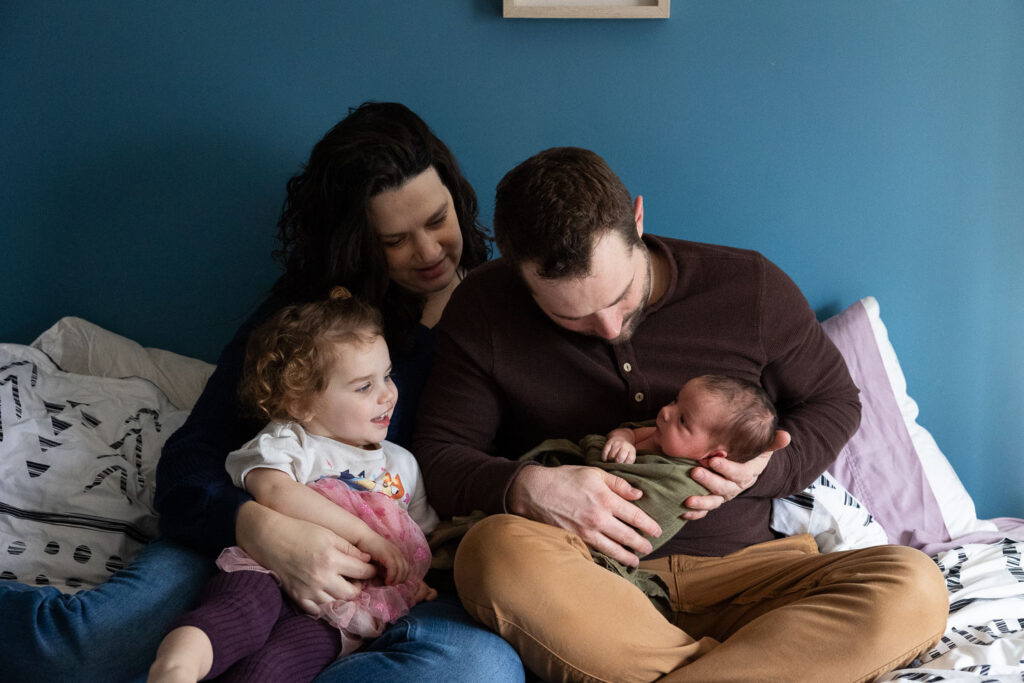 family cuddles on bed with toddler daughter and newborn son during Raleigh newborn photo session at home