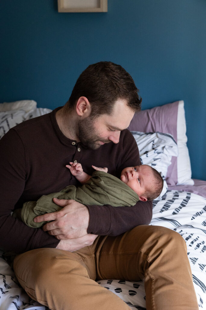Natural newborn photos in Raleigh, NC, dad smiles at newborn son while holding him in green swaddle blanket
