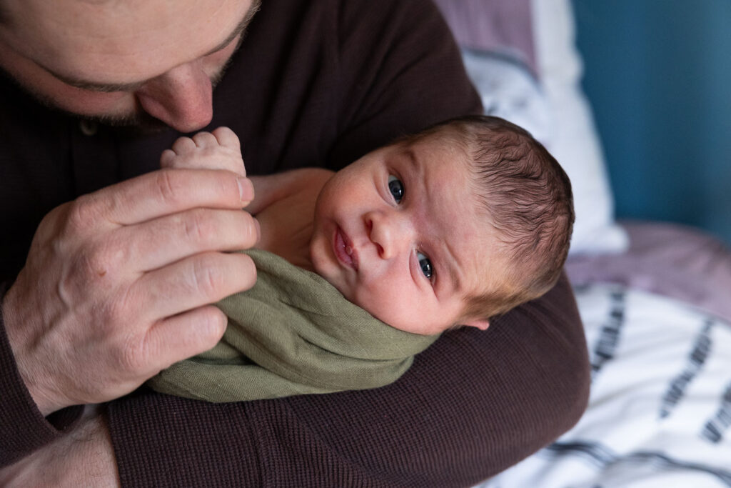 Raleigh natural newborn photo session at home, dad holds newborn son with one arm while holding his hand 