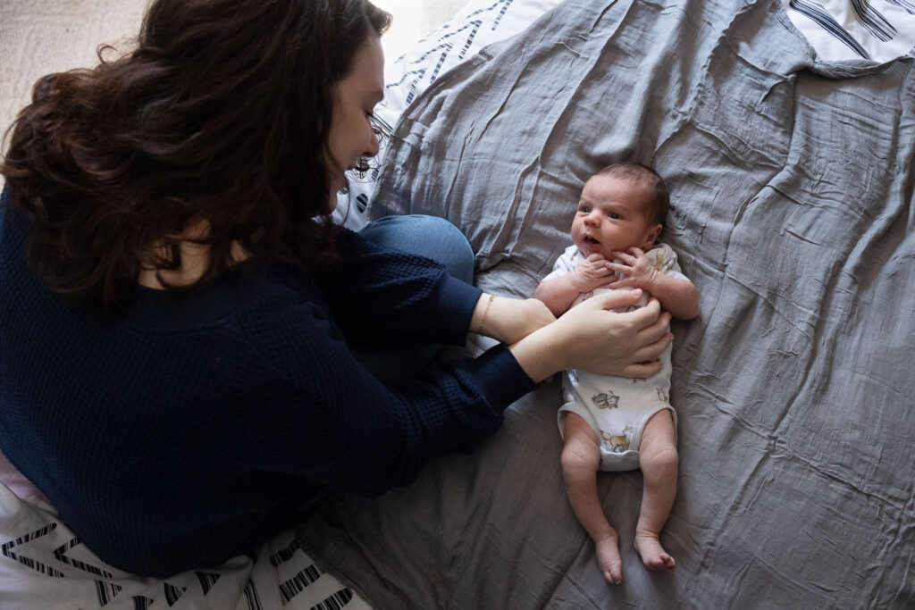 Newborn baby in onesie looks up at his mom during candid newborn session in Raleigh, NC