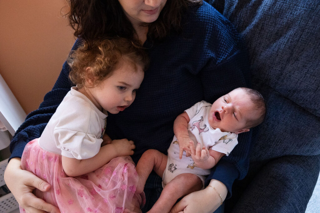 Raleigh newborn session at home, mom holds toddler daughter and newborn son in her glider in the nursery