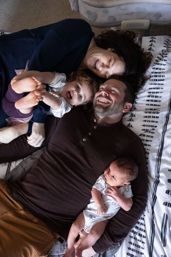 View from above as family of four lays on their back on parents' bed during Raleigh newborn session