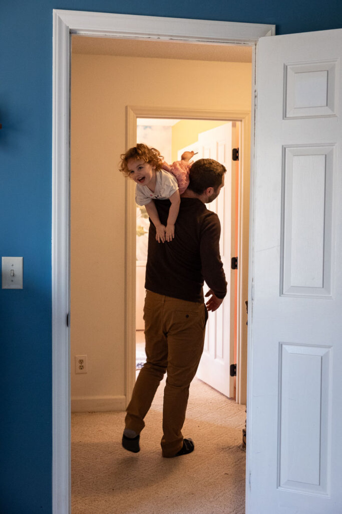 Candid family photo session in Raleigh, NC, dad carries toddler daughter over his shoulder