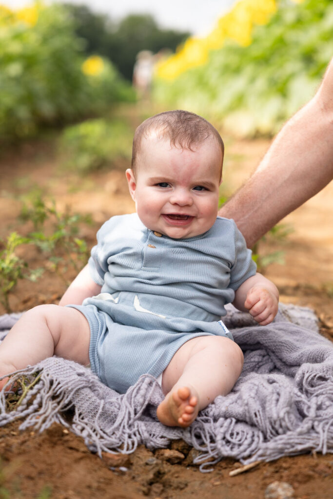 3-month-old baby milestone photo session in Raleigh, NC at Dorothea Dix Park sunflower field, baby smiles big at camera
