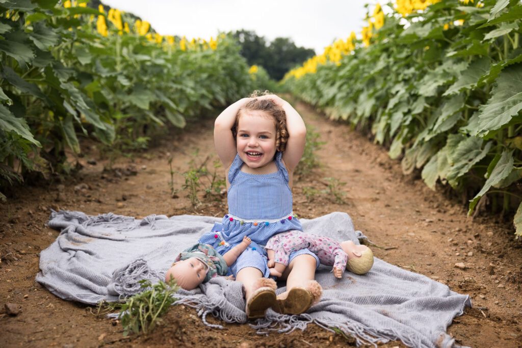Toddler girl sits between rows of sunflowers at Dorothea Dix Park family photo session