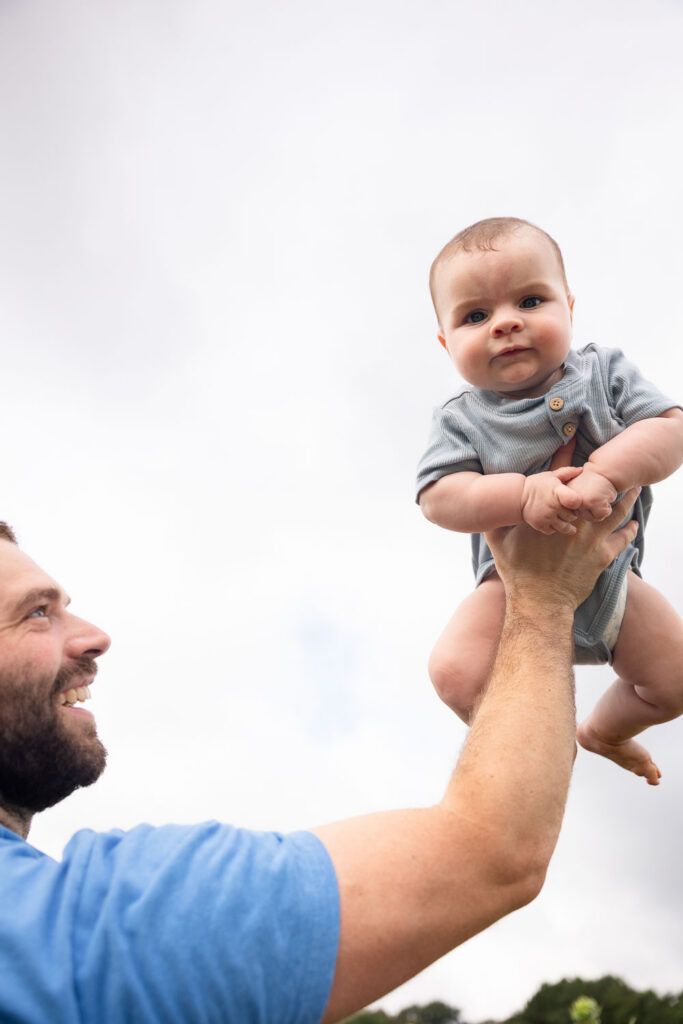 Dad holding 6-month-old baby up with one hand at Dix Park sunflower field photo session