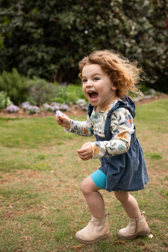 Very excited toddler girl running with flower at Fred Fletcher Park Raleigh photo session