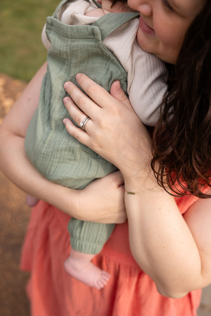 Close-up of Mom's hand with wedding ring as she holds her 3-month-old son during a baby milestone photo session