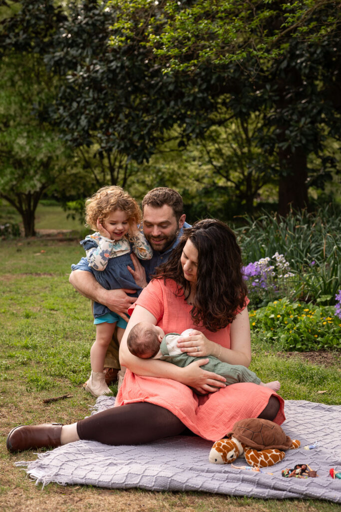 Fred Fletcher Park baby photo session with toddler, family sits on blanket and looks at baby in mom's arms