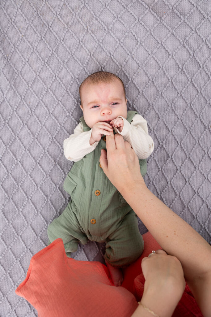 View from above of 3-month-old baby boy as he lays on a grey blanket during his baby milestone photo session in Raleigh