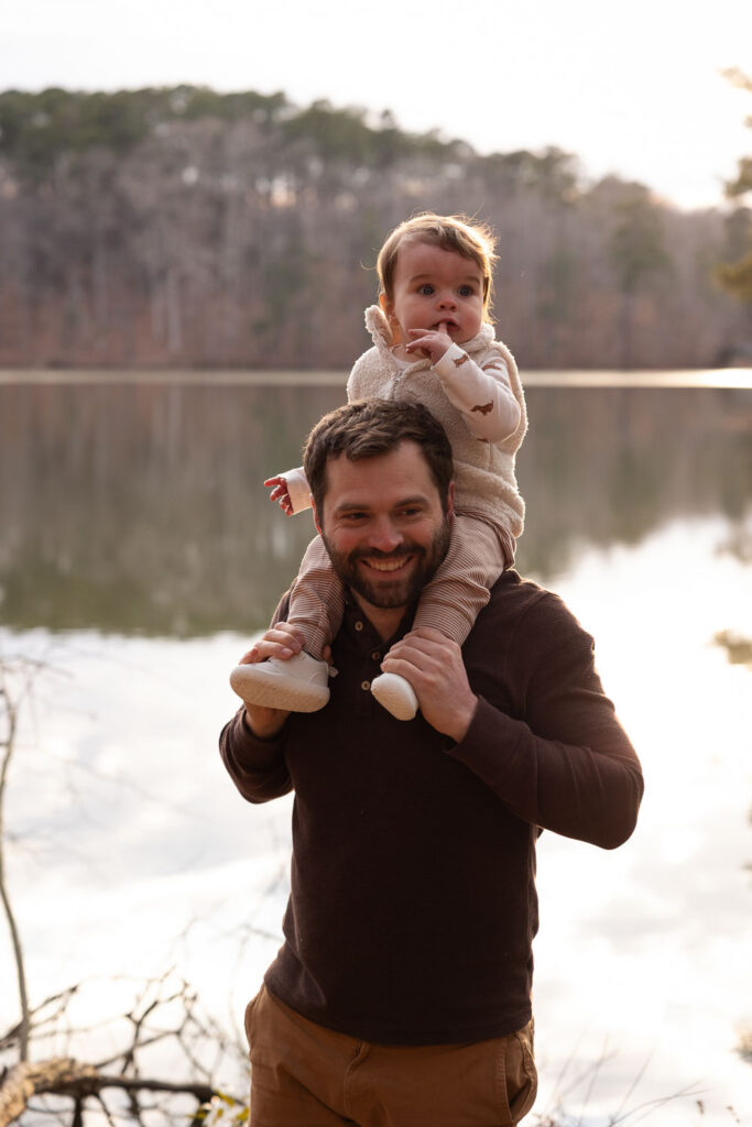 Dad and 1-year-old son in golden light with lake in the background at Lake Johnson Raleigh family photo session