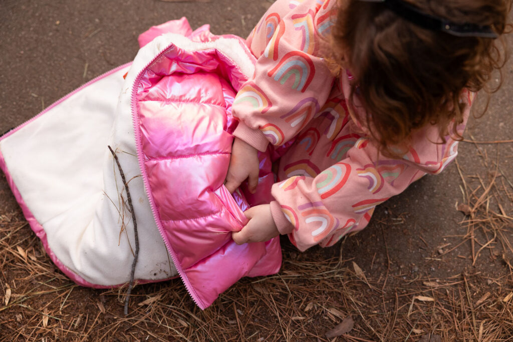 View from above as toddler girl dutifully tucks rocks into her coat pocket