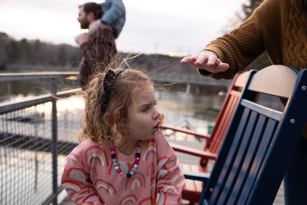 Static electricity hair as toddler girl sits in chair at Lake Johnson Raleigh family photo session