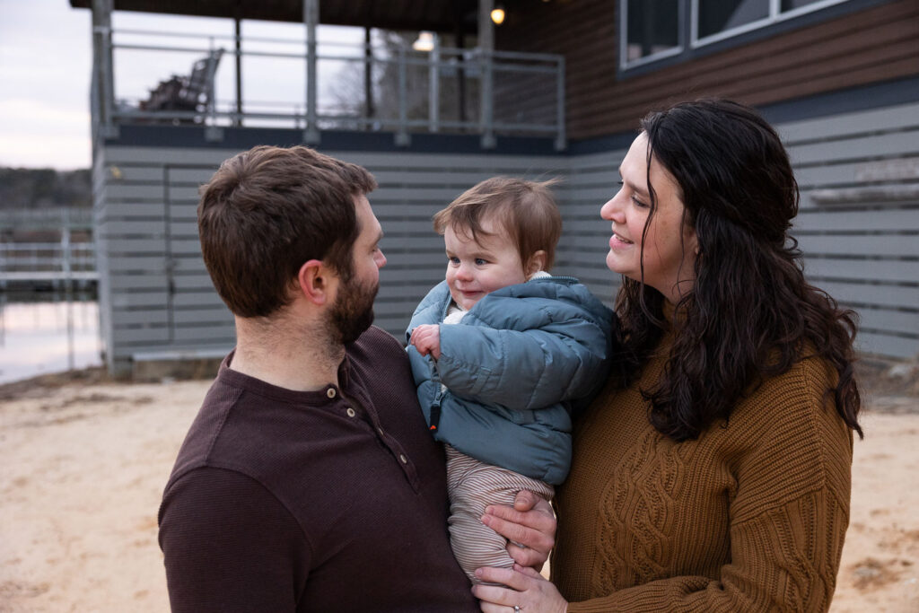 Lake Johnson photo session on boat launch beach, mom and dad hold baby and look at each other
