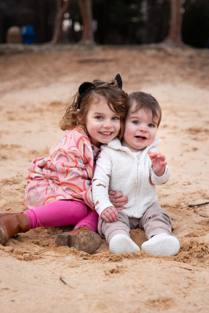 Toddler girl hugs close to baby brother during 1-year-old photo session at Lake Johnson in Raleigh