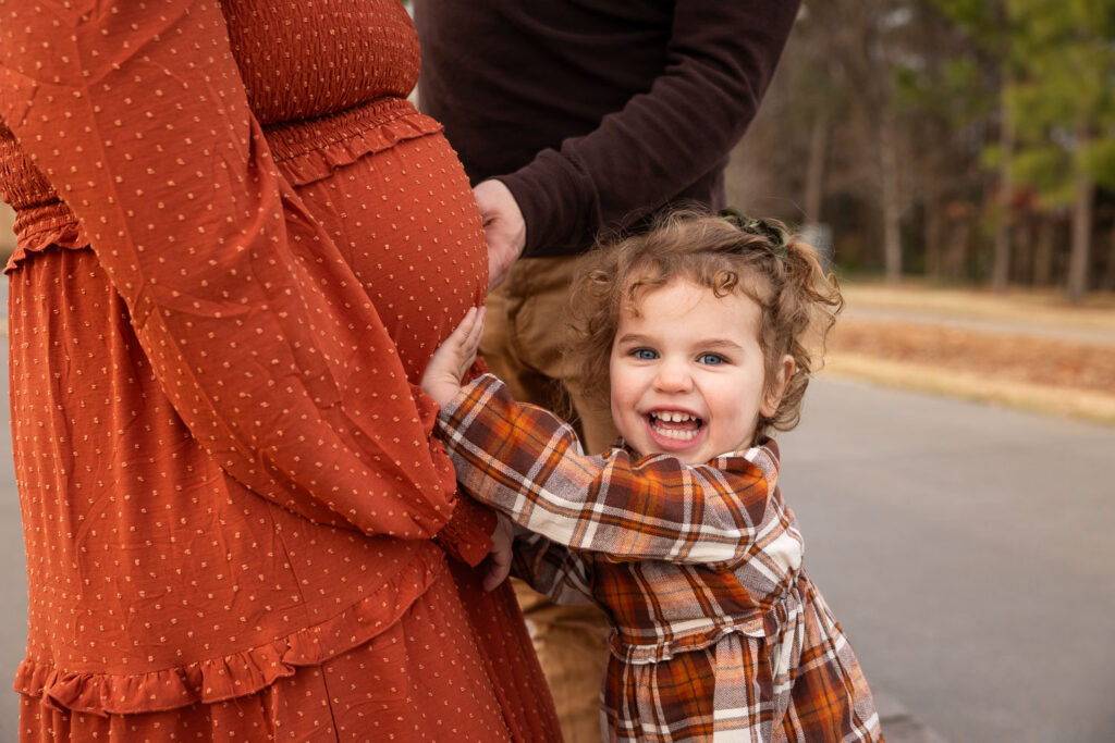Toddler smiling pushing on mommy's baby belly