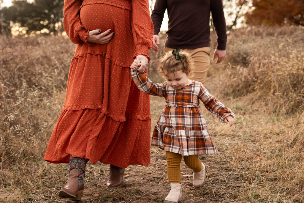 Raleigh maternity portraits with toddler, family walking toward camera with mom cupping baby belly and holding daughter's hand