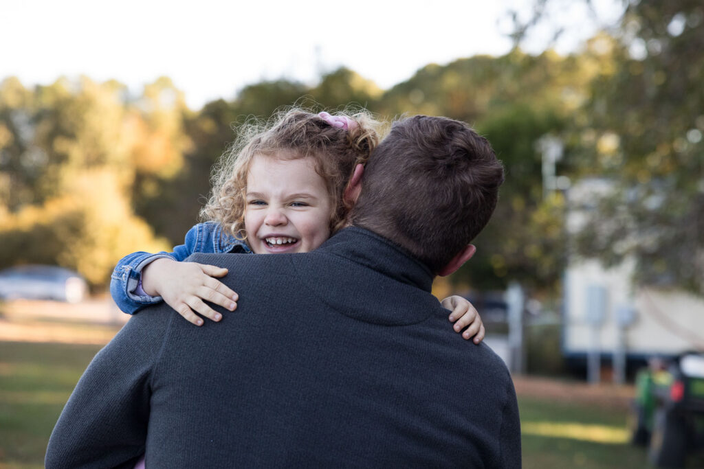 Prairie Ridge Ecostation family photo session, girl is carried by her dad and smiles big as he walks away from camera
