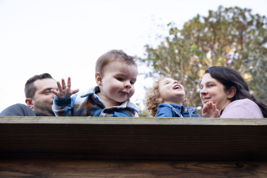 Family of four at Prairie Ridge Ecostation, camera looks up from below wooden railing to see the family