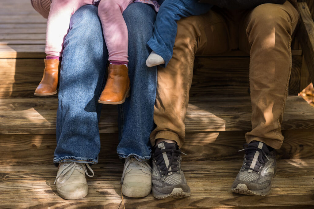 Close-up on legs and shoes as family sits together and reads at Prairie Ridge Ecostation family photo session