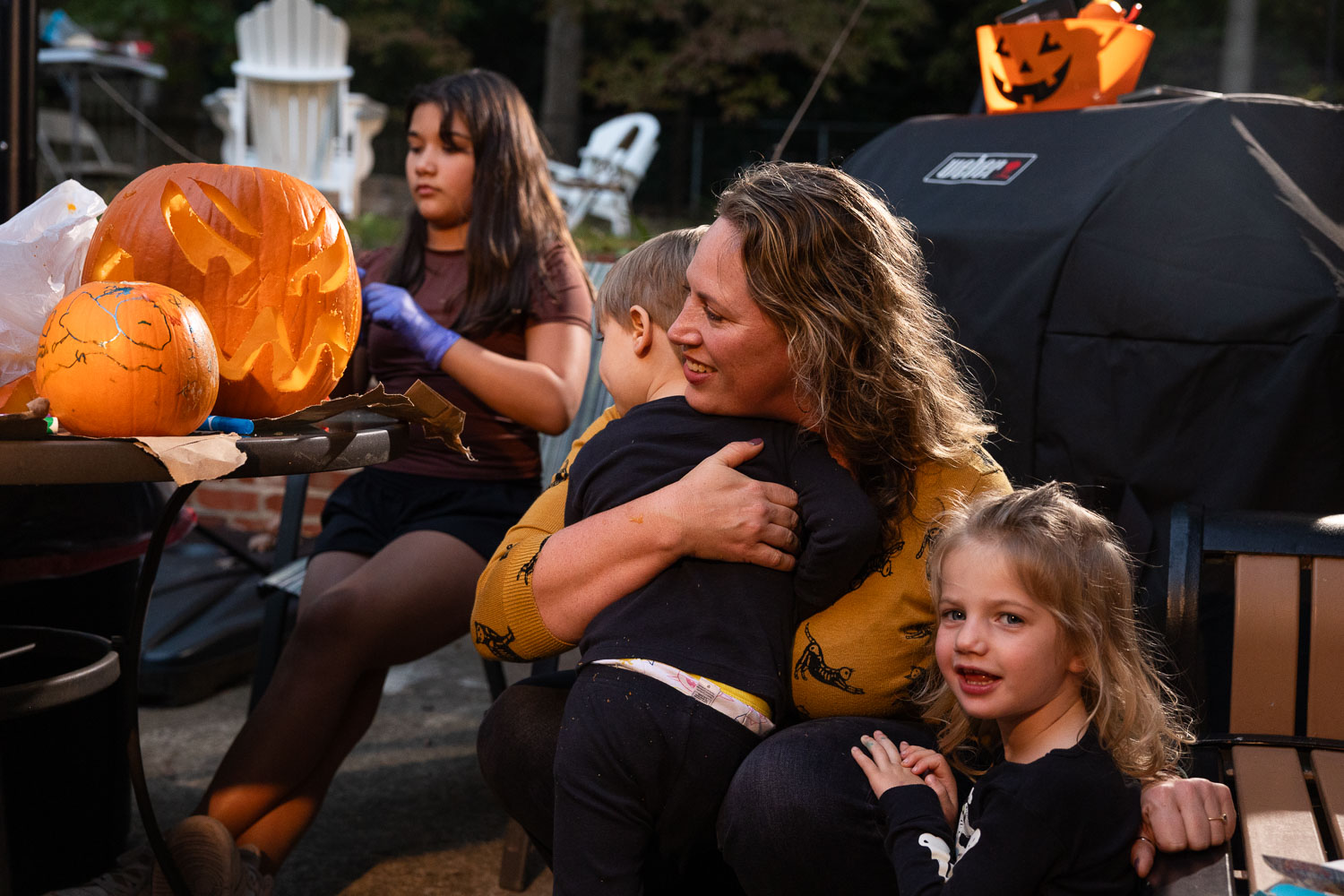 Raleigh candid mini-session capturing pumpkin carving as a family to preserve these moments. A mom hugs her toddler twins by the pumpkin carving table.