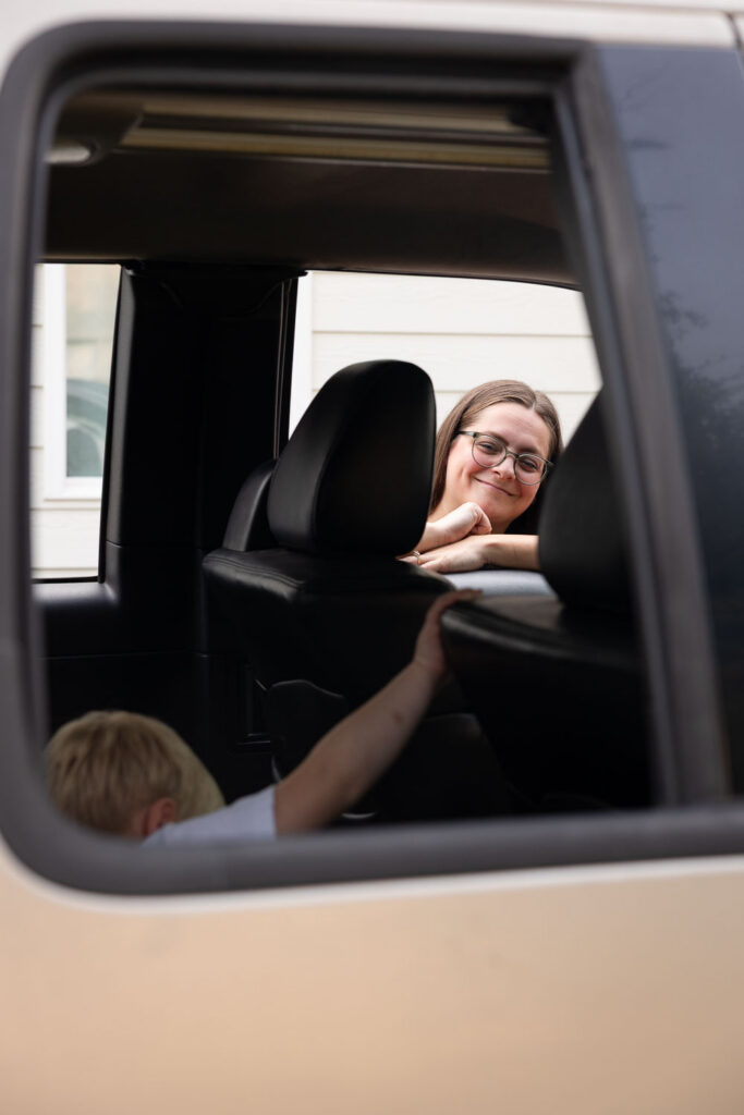 Mom smiling through the open car window as her young son sits in the back seat.