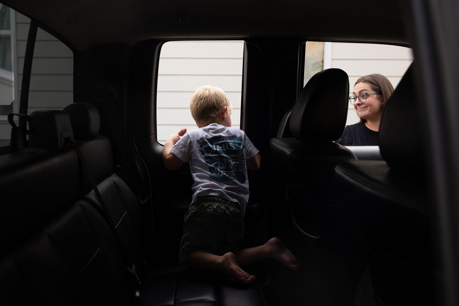 Young boy looking through the back seat window of the family car during an at-home documentary family photo session.