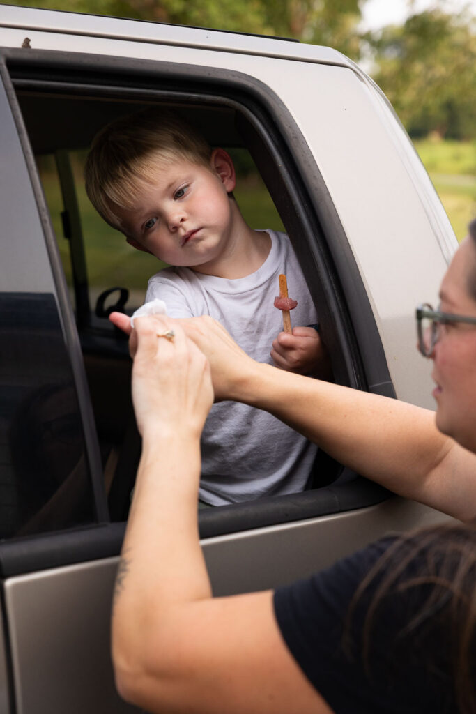 Mom reaching through the truck window to clean the hands of her young son through the open window.