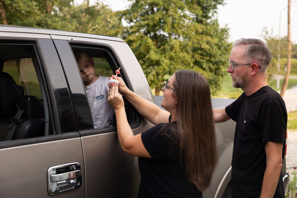 Mom and dad cleaning the hands of their young son at the open car window outside their Holly Springs home.