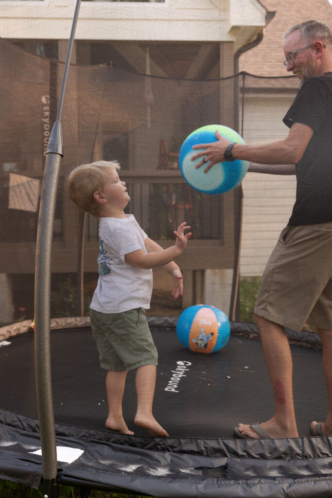 Dad and young son playing with colorful balls on the backyard trampoline.