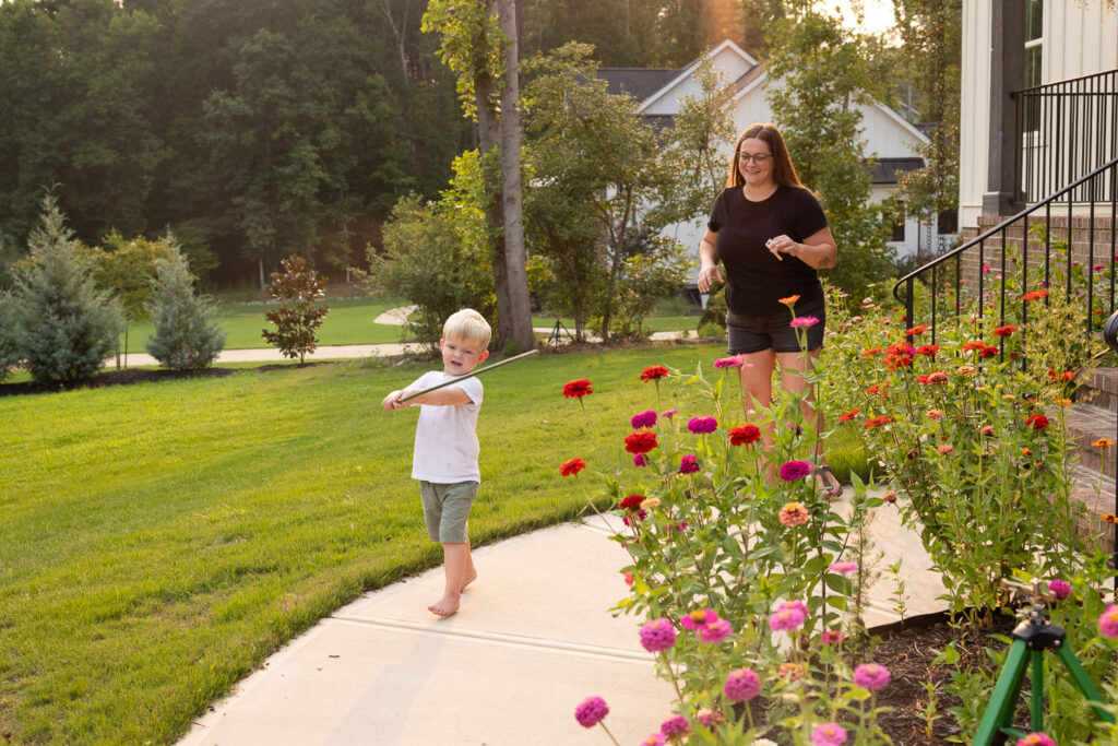 Young boy walking ahead of mom along the sidewalk beside the family’s flower garden.