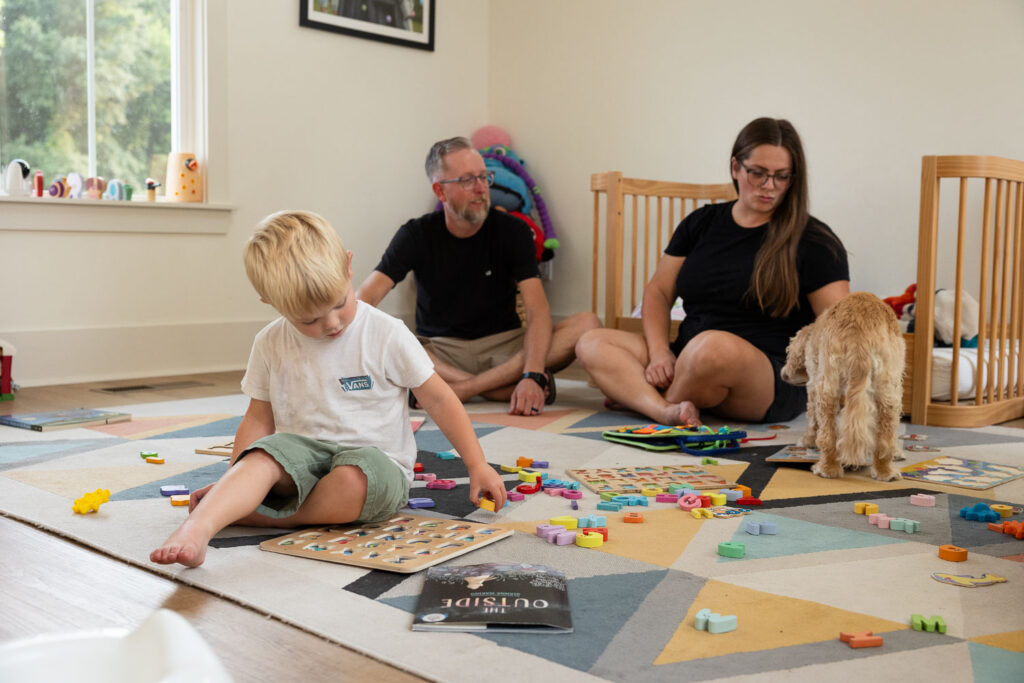 Mom, dad, and young son sitting on a kids' bedroom floor playing with toys together.