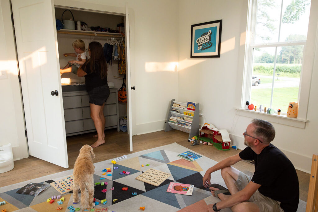 Wide view of a family playing with toys on a bedroom room floor during an at-home family photo session.