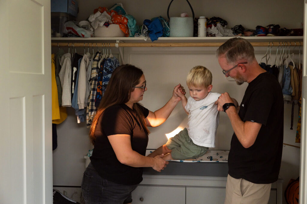 Mom and dad interacting with their young son at a closet table at home.