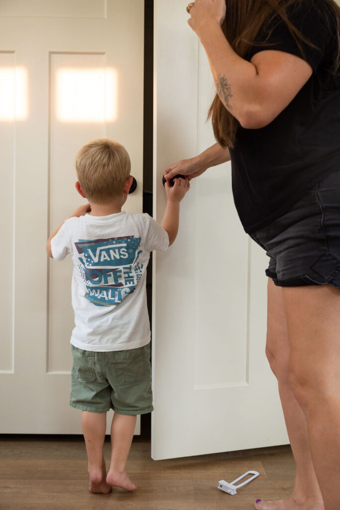 Young boy beginning to open a closet door while his mom stands alongside him.