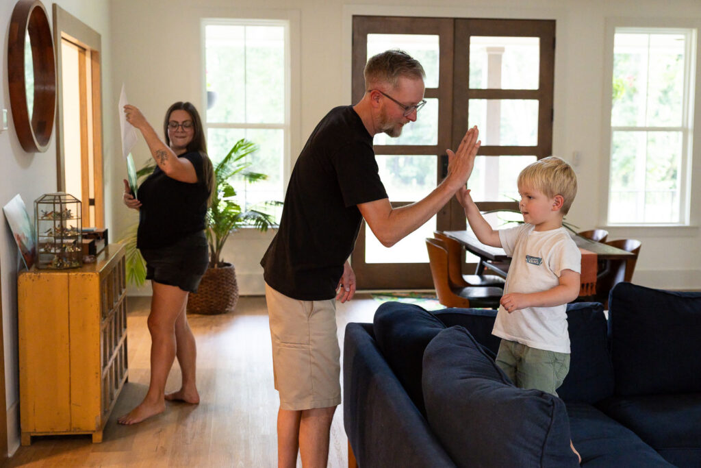 Mom, dad, and young son playing together in the living room of their home while mom starts to put a record in the record player and dad and son high-five.