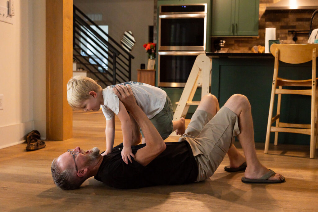 Dad lying on the floor while his young son clambers over him during playful family time.