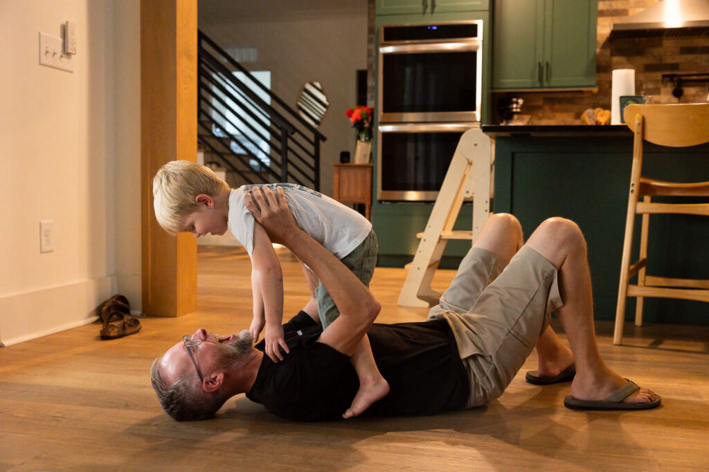 Young boy leaning over dad as they play together on the hardwood floor.