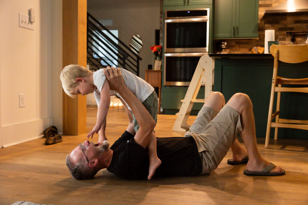 Dad and young son laughing and playing on the floor at home.
