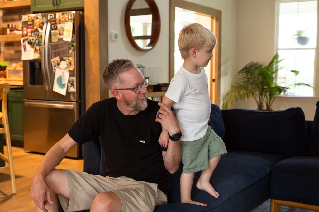 Dad sitting on the couch with his young son beside him during a relaxed family moment.