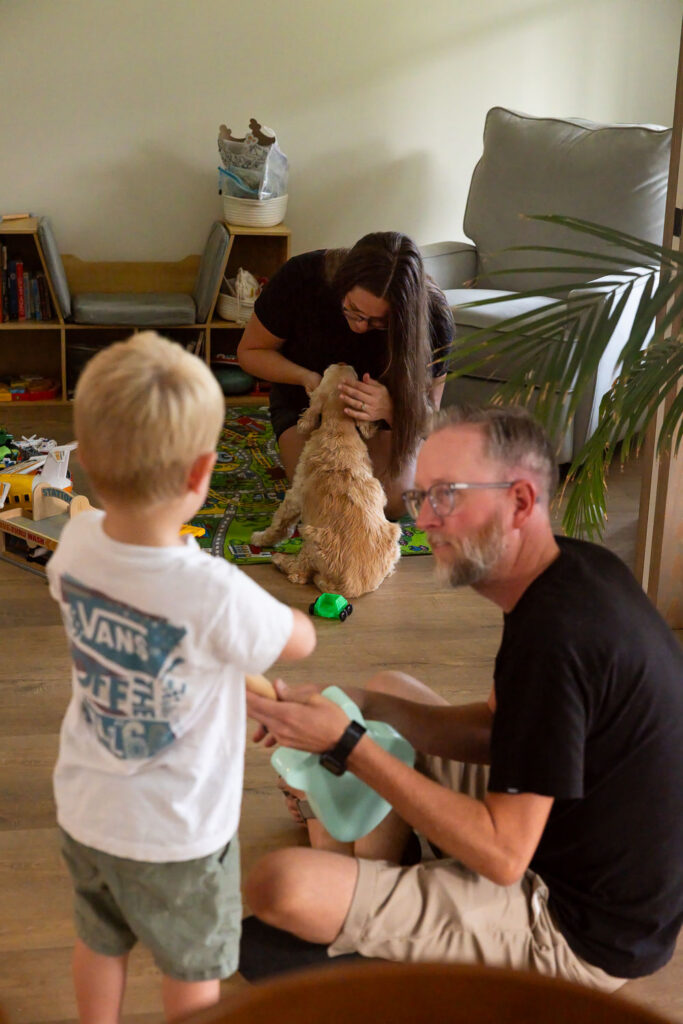 Dad playing with his young son while mom sits with the dog nearby in the family playroom.